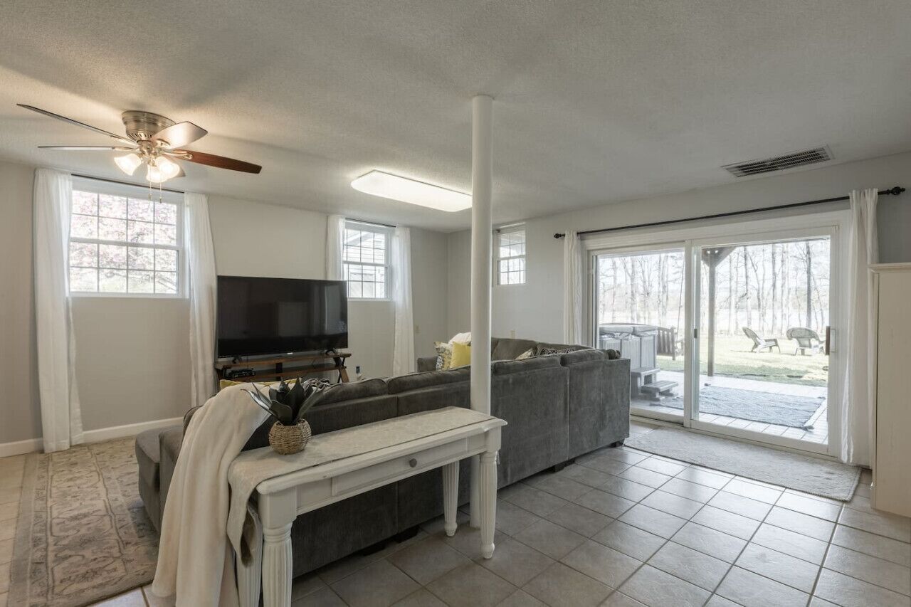 A spacious living room with a large gray sectional sofa, a flat-screen TV, a ceiling fan, and a sliding glass door leading to a backyard.