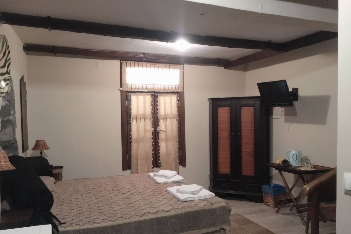 A bedroom with a bed, a desk, a wardrobe, a television, and a window with curtains.