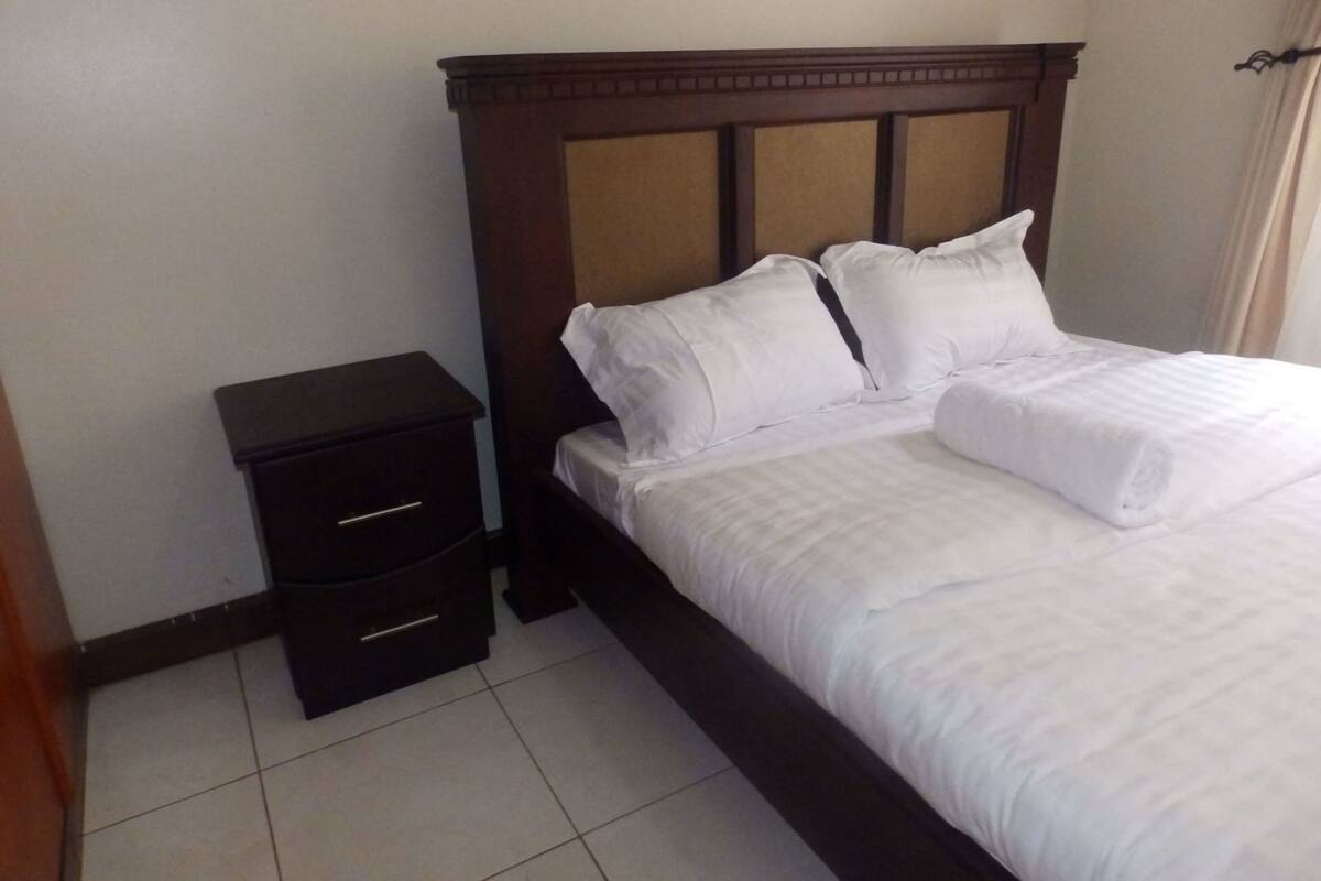 A hotel room with a wooden headboard, a single bed with white bedding, and a small bedside table with drawers.