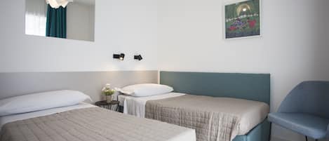 Une chambre d’hôtel avec deux lits, une chaise, une petite table sur laquelle est posé un vase de fleurs, un tableau au mur et un miroir au-dessus du lit.