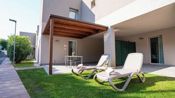Un área de estar moderna al aire libre con dos sillones, una mesita y un porche cubierto.