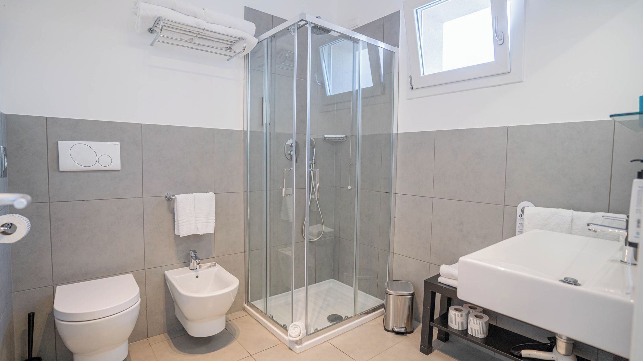 Ein modernes Badezimmer mit einer gläsernen Duschkabine, einem Bidet, einer Toilette und einem Waschbecken mit Spiegel.
