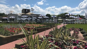 Un hotel con posti a sedere all'aperto sotto ombrelloni a righe, un giardino con fiori colorati e un cielo azzurro limpido.