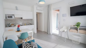 Un appartamento moderno con cucina, zona pranzo e soggiorno. Dispone di una TV a schermo piatto, un tavolo da pranzo con sedie, un divano e un piccolo tavolino con una pianta.