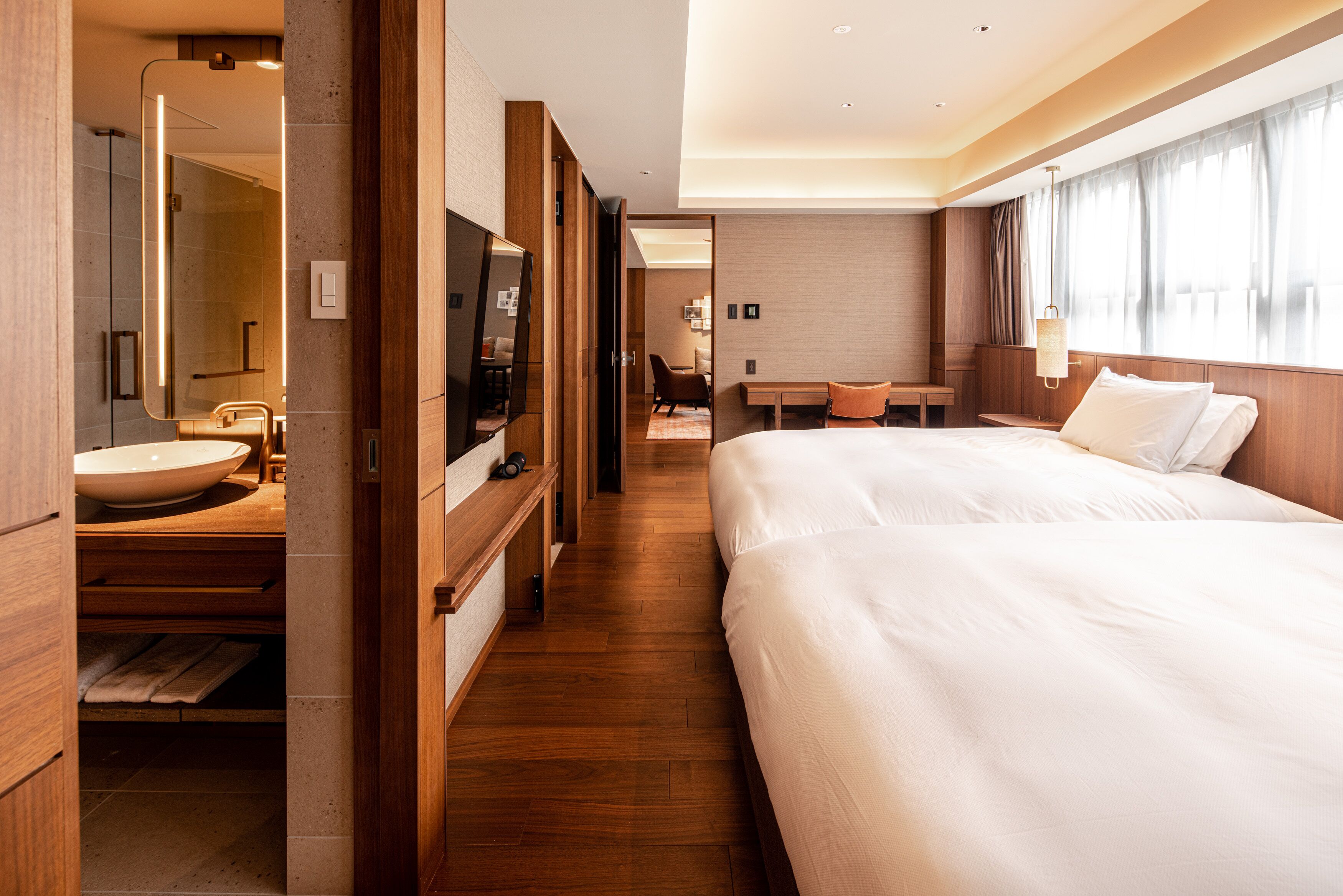 A hotel room with a large bed, a sitting area with a table and chairs, a bathroom with a sink and mirror, and a TV.
