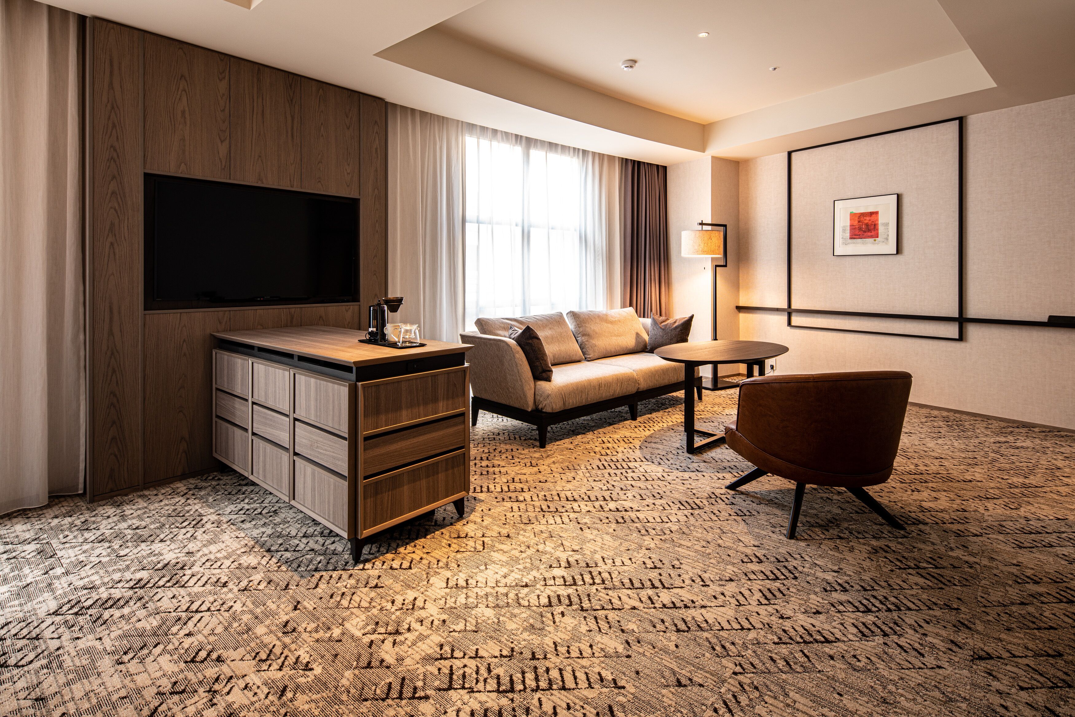 Habitación de hotel con televisor de pantalla plana, sofá, sillón, escritorio y lámpara.