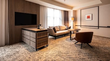 Habitación de hotel con televisor de pantalla plana, sofá, sillón, escritorio y lámpara.