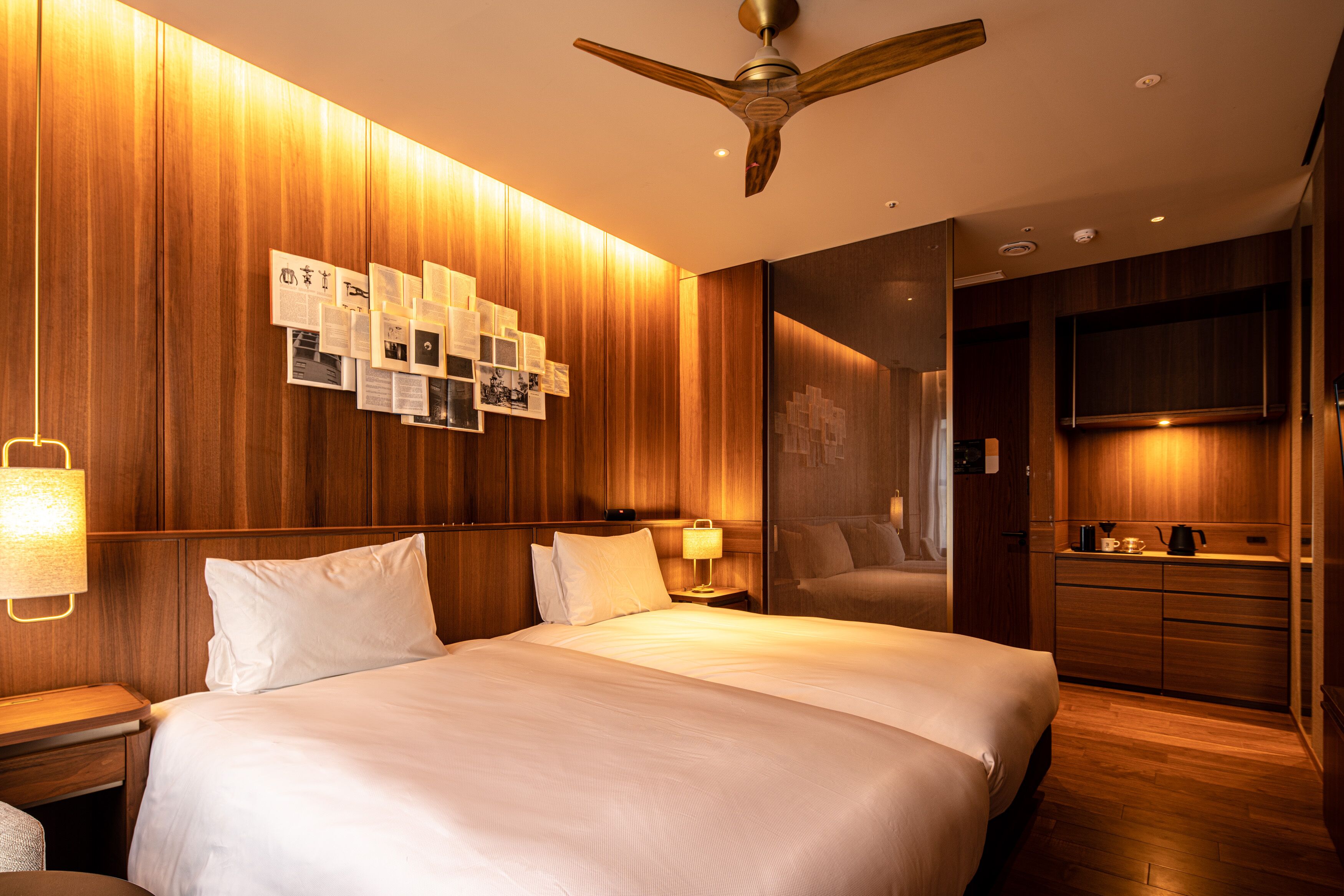 A hotel room with a large bed, wooden panel walls, a ceiling fan, a bedside table with a lamp, a mirror, and a TV mounted on the wall.