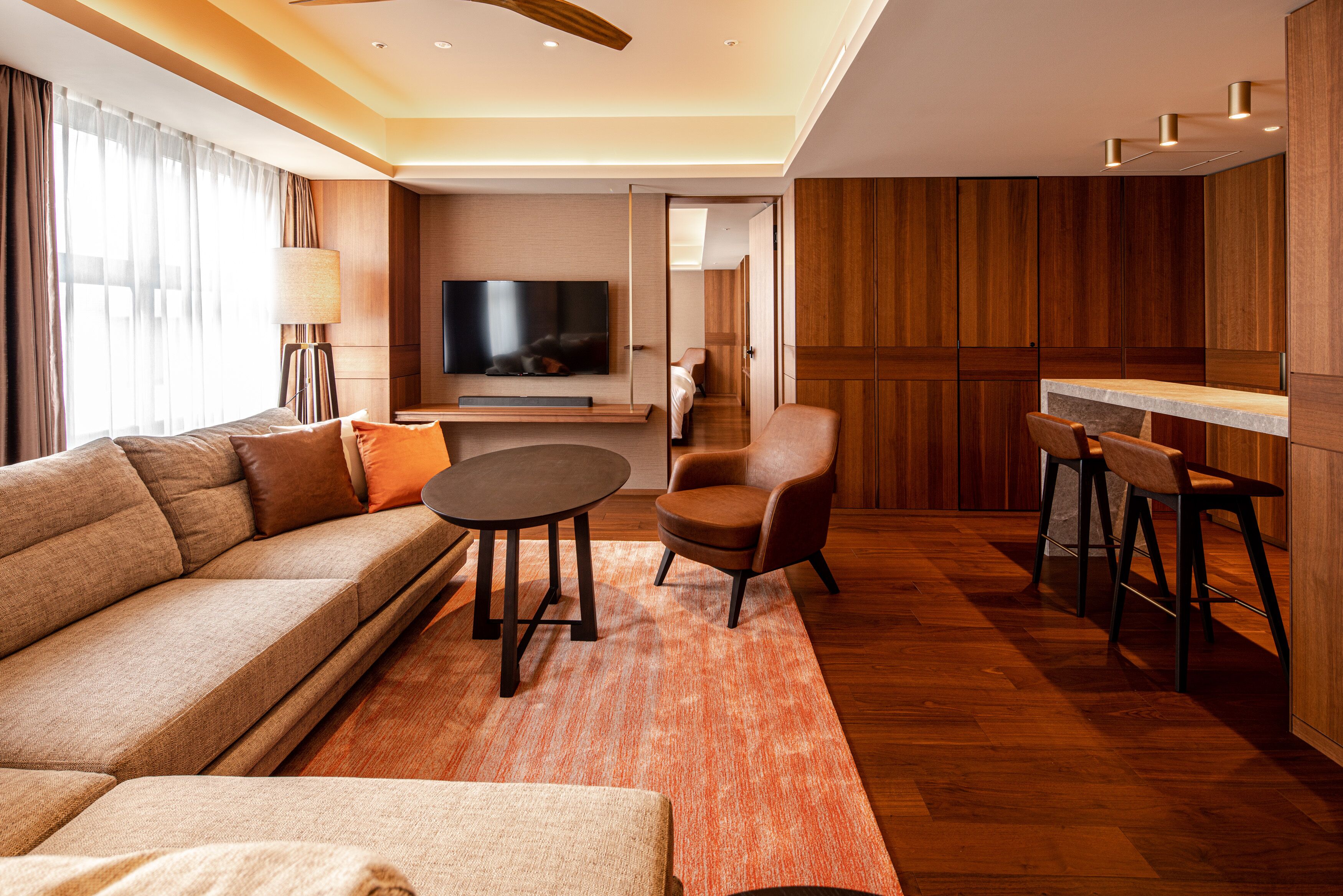 Ein modernes Wohnzimmer mit einer Couch, einem Sessel, einem runden Tisch und einem an der Wand befestigten Fernseher.