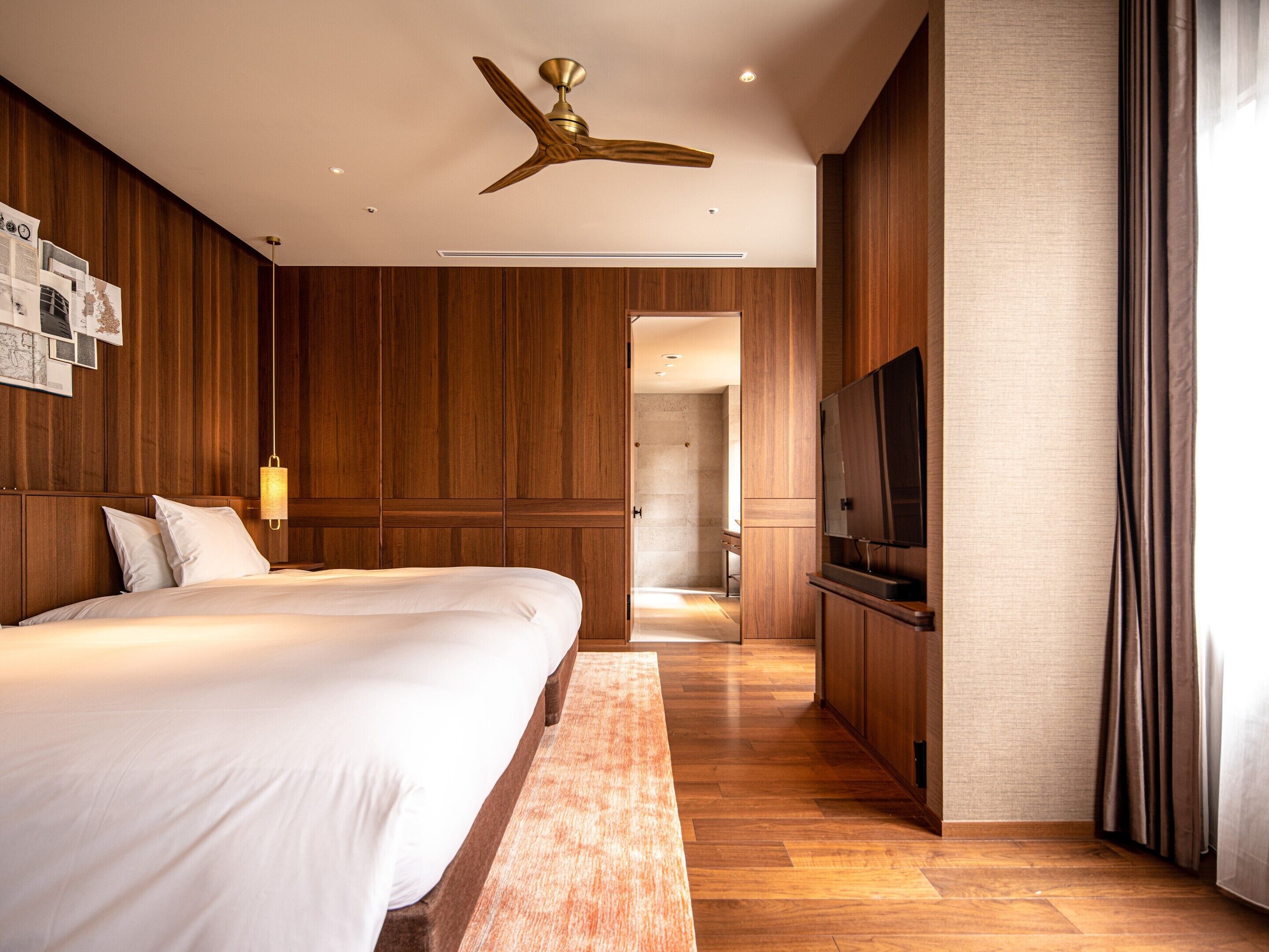 A modern hotel room with a large bed, wooden paneling, a ceiling fan, a flat-screen TV, and a wooden bench.