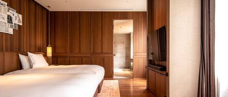 A modern hotel room with a large bed, wooden paneling, a ceiling fan, a flat-screen TV, and a wooden bench.