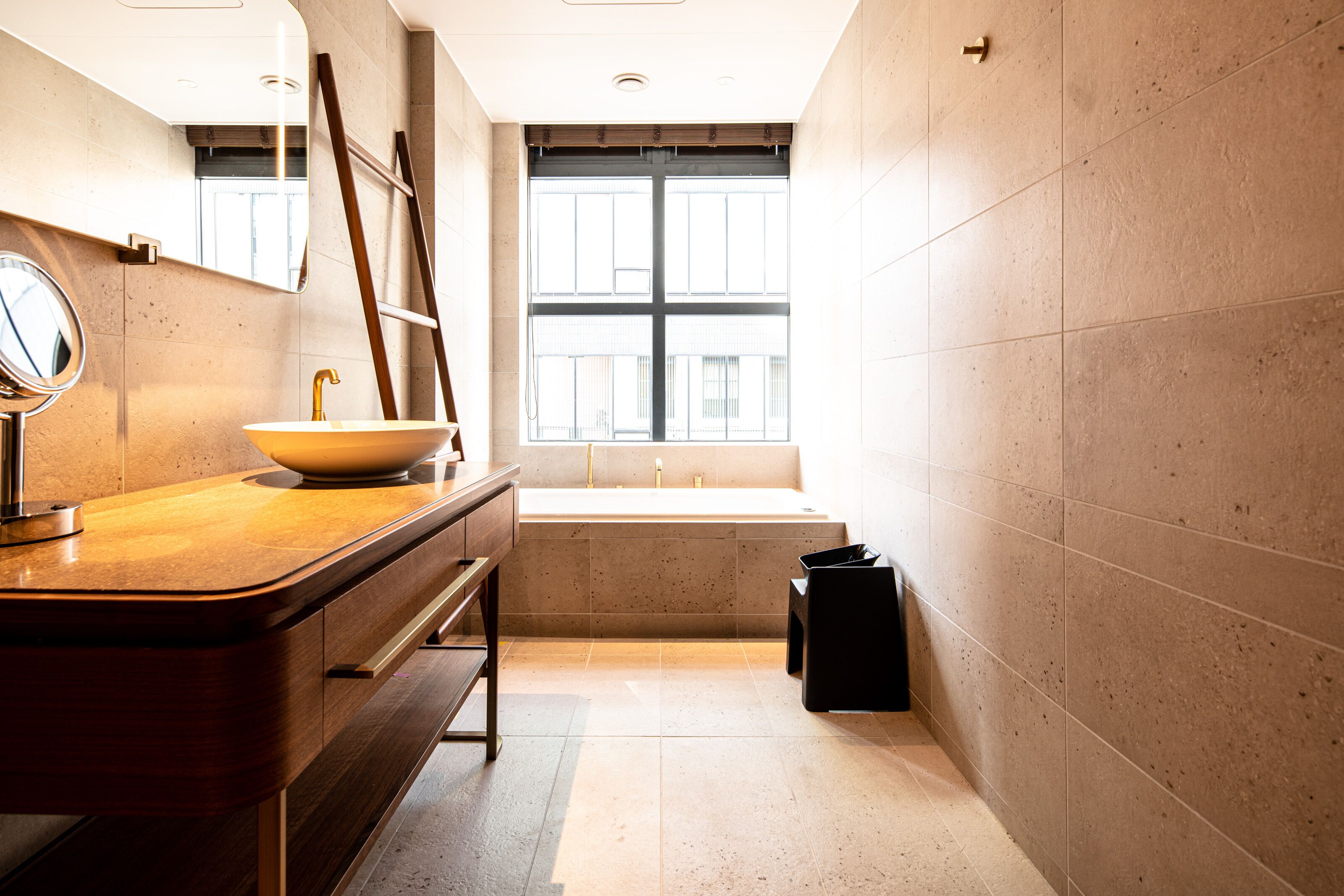 A modern bathroom with a wooden vanity, a round mirror, a sink, and a bathtub.