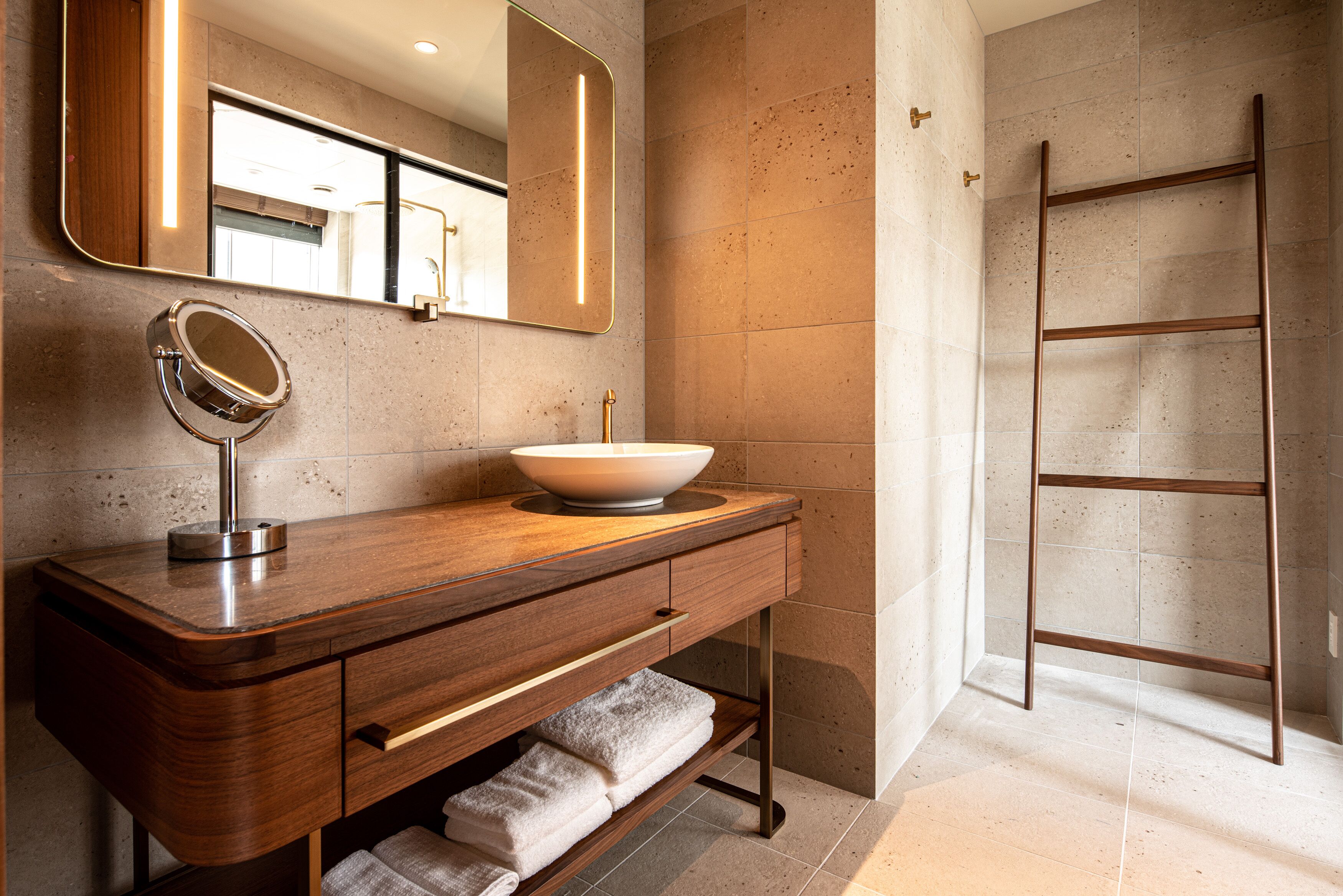 Une salle de bain moderne avec un meuble-lavabo en bois, un grand miroir, un lavabo sur colonne et une échelle en métal adossée au mur.