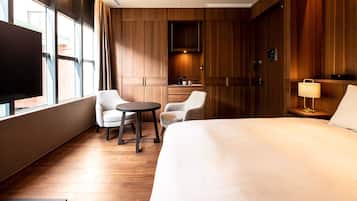 A hotel room with a large bed, two armchairs, a small table, a TV, and a wooden wardrobe.