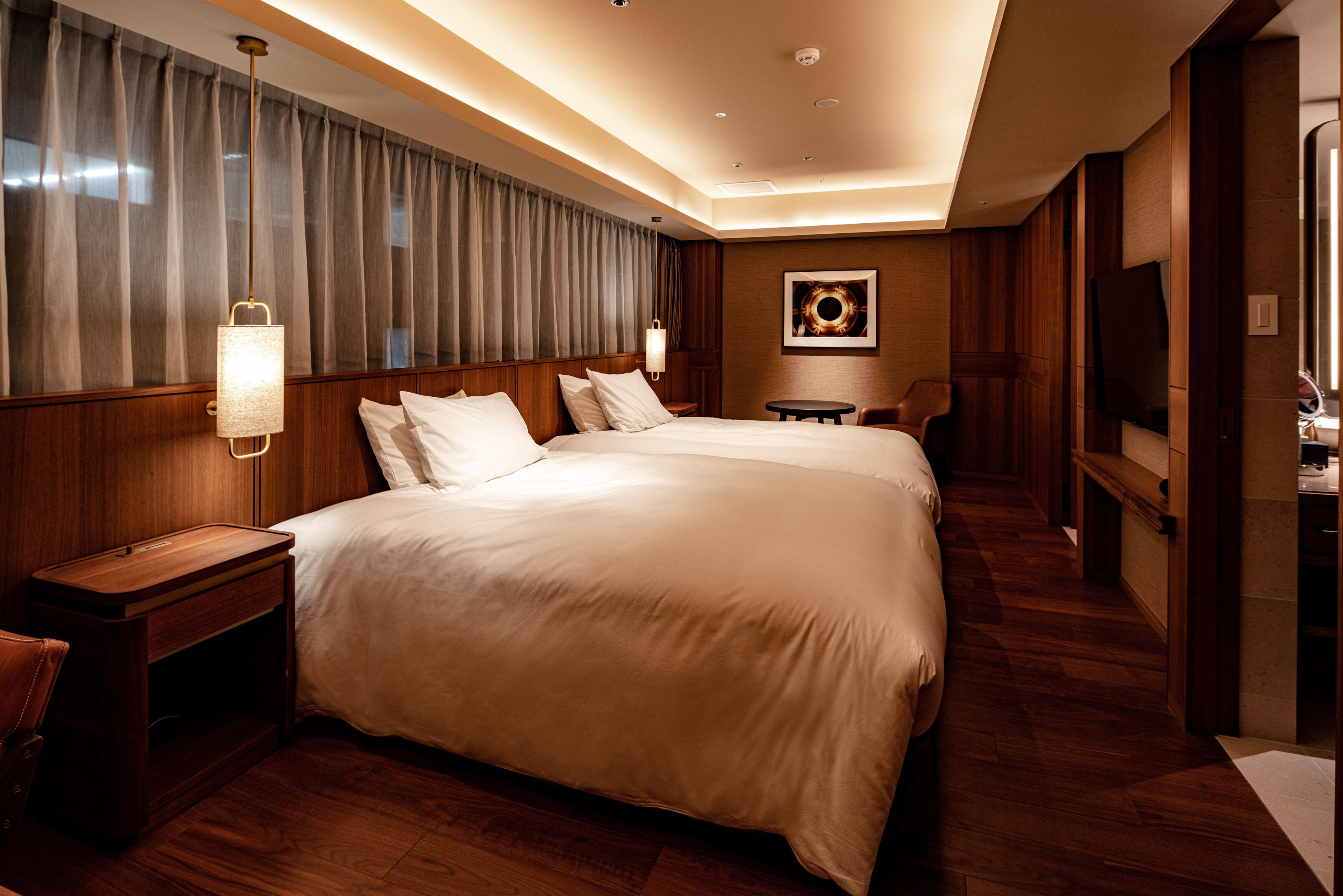 Een hotelkamer met een groot bed, een houten hoofdbord, nachtkastjes, een bureau, een stoel, een televisie en een kunstwerk aan de muur.
