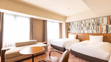 A hotel room with two beds, a sofa, a small table, and a bookshelf.