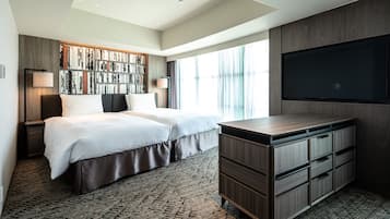 A modern hotel room with a large bed, a built-in bookshelf, a flat-screen TV, and a desk with drawers.