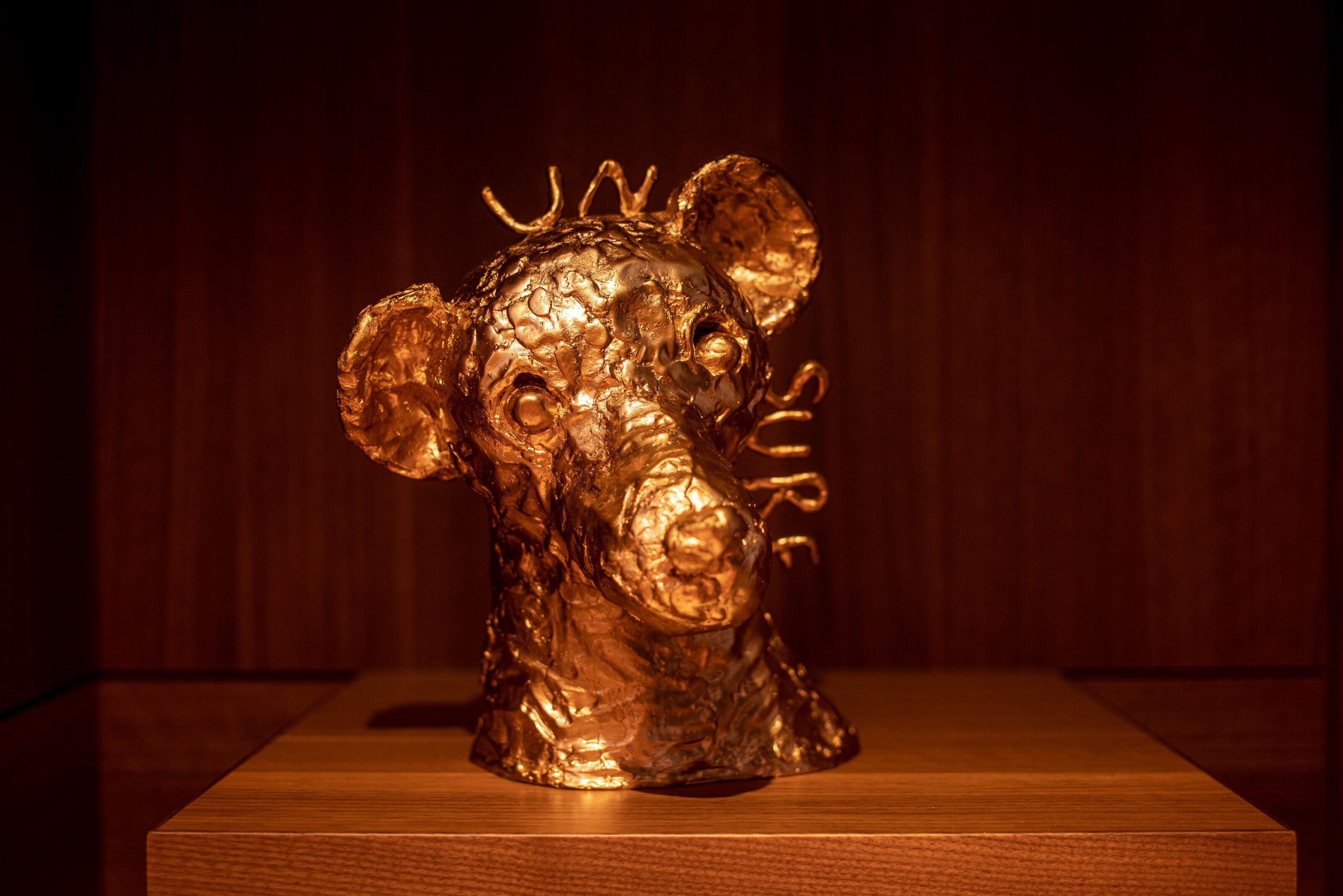Une sculpture dorée représentant la tête d’un taureau, avec le mot « TAUREAU » inscrit sur le côté, placée sur une plateforme en bois.
