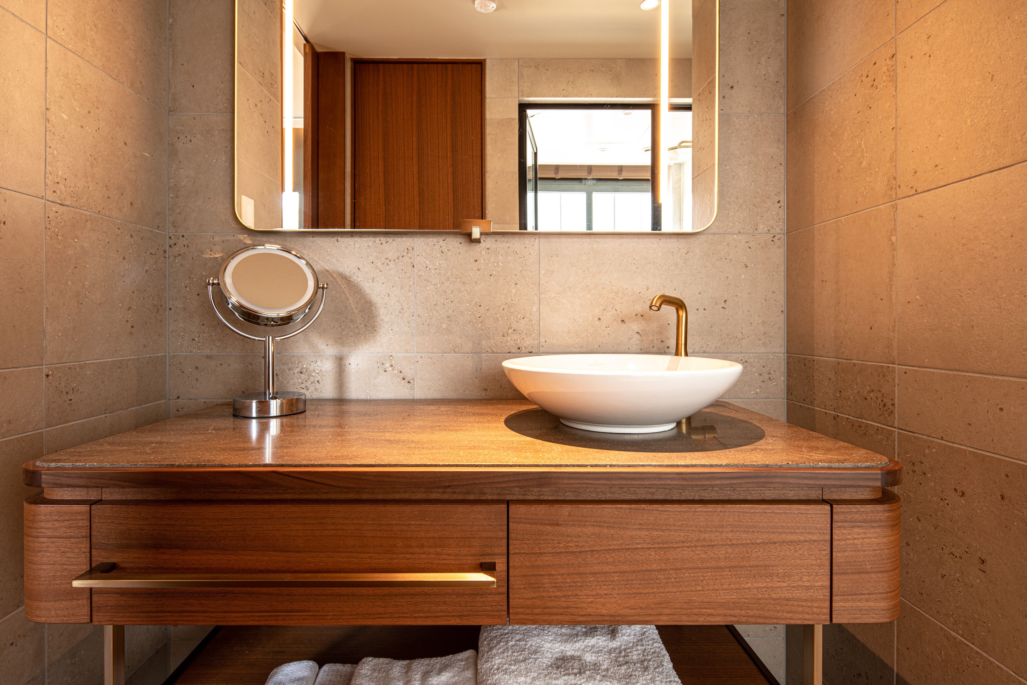 A modern bathroom with a wooden vanity, a round mirror, and a vessel sink.