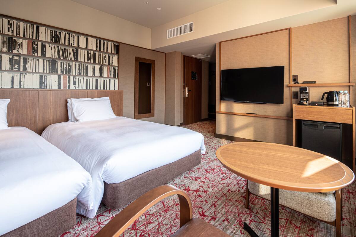 A hotel room with two beds, a TV, a coffee machine, and a small table.