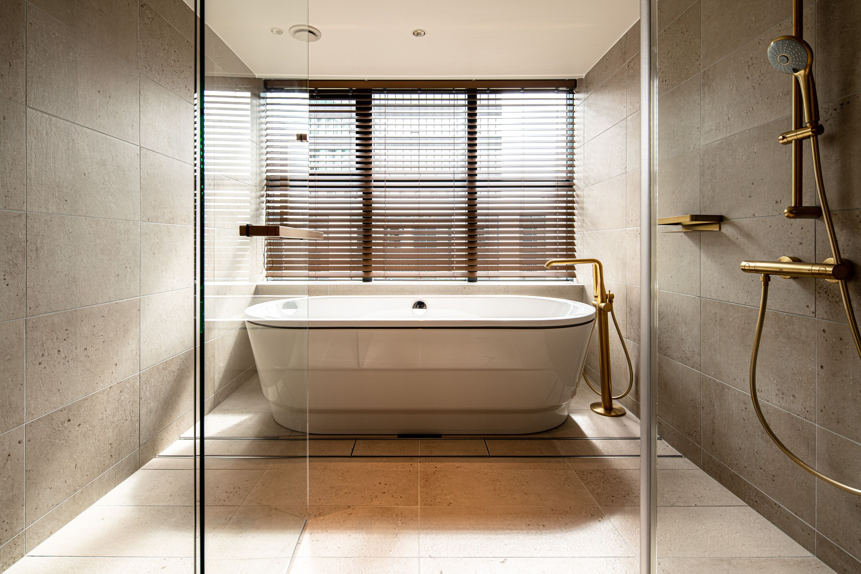A modern bathroom with a freestanding bathtub, a glass shower enclosure, and a window with blinds.