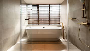 A modern bathroom with a freestanding bathtub, a glass shower enclosure, and a window with blinds.