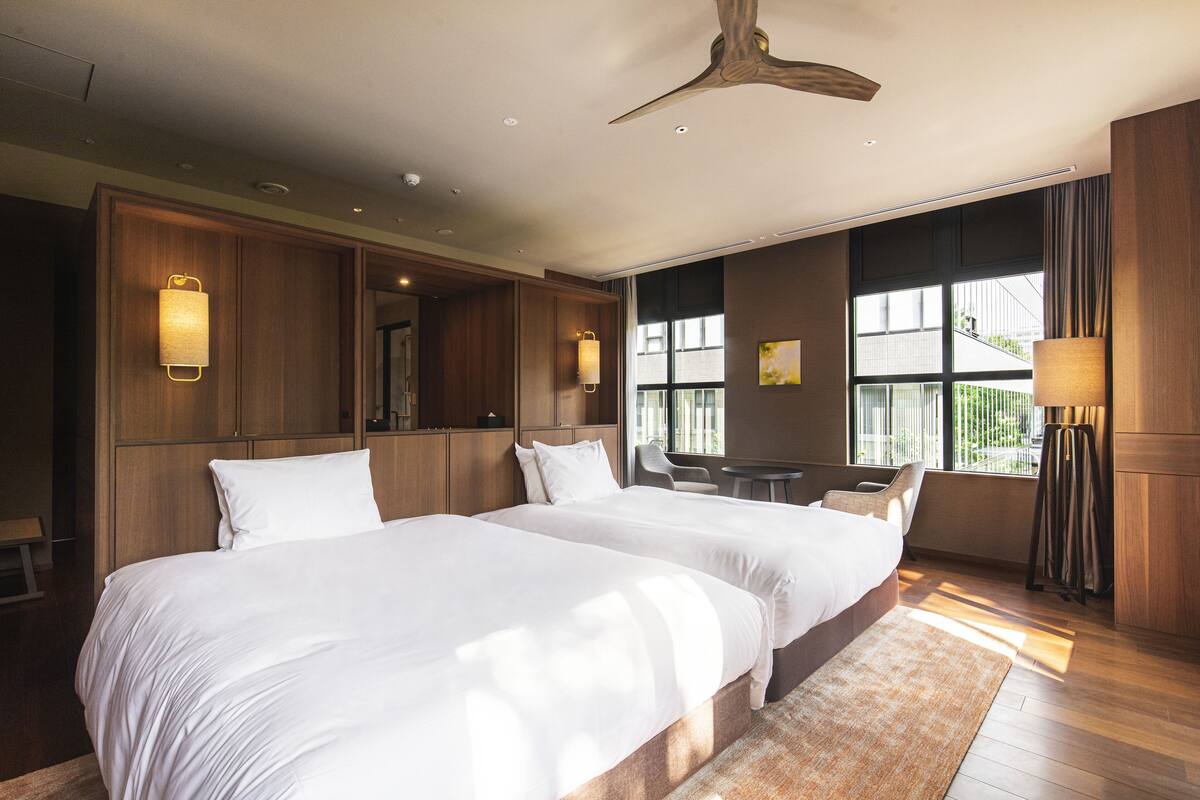 A hotel room with two large beds, a ceiling fan, and a large window providing a view of the outdoors.