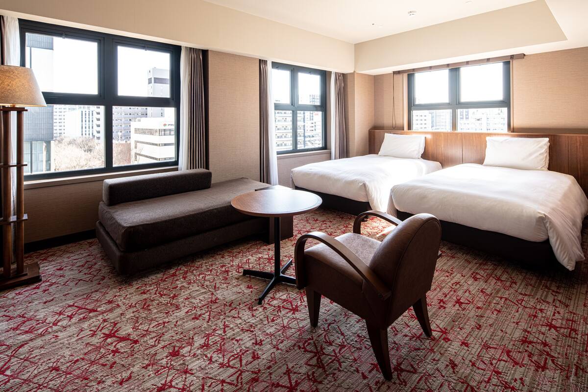 A hotel room with two beds, a sofa, a small table, and a chair.