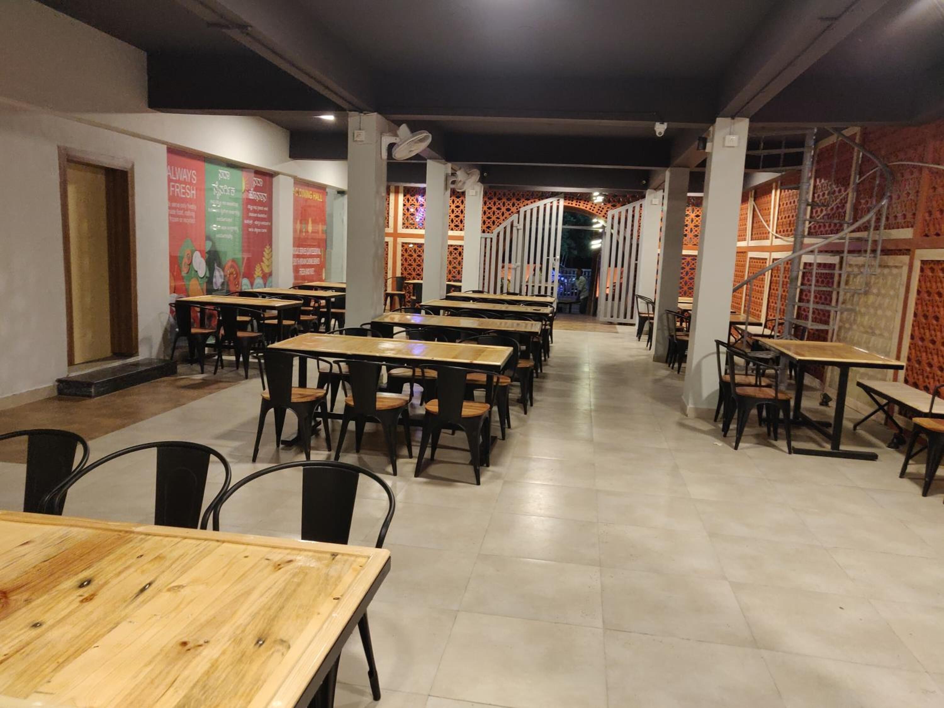 Een ruime eethoek binnen, met meerdere houten tafels en zwarte stoelen, met een betegelde vloer en decoratieve wandpanelen.