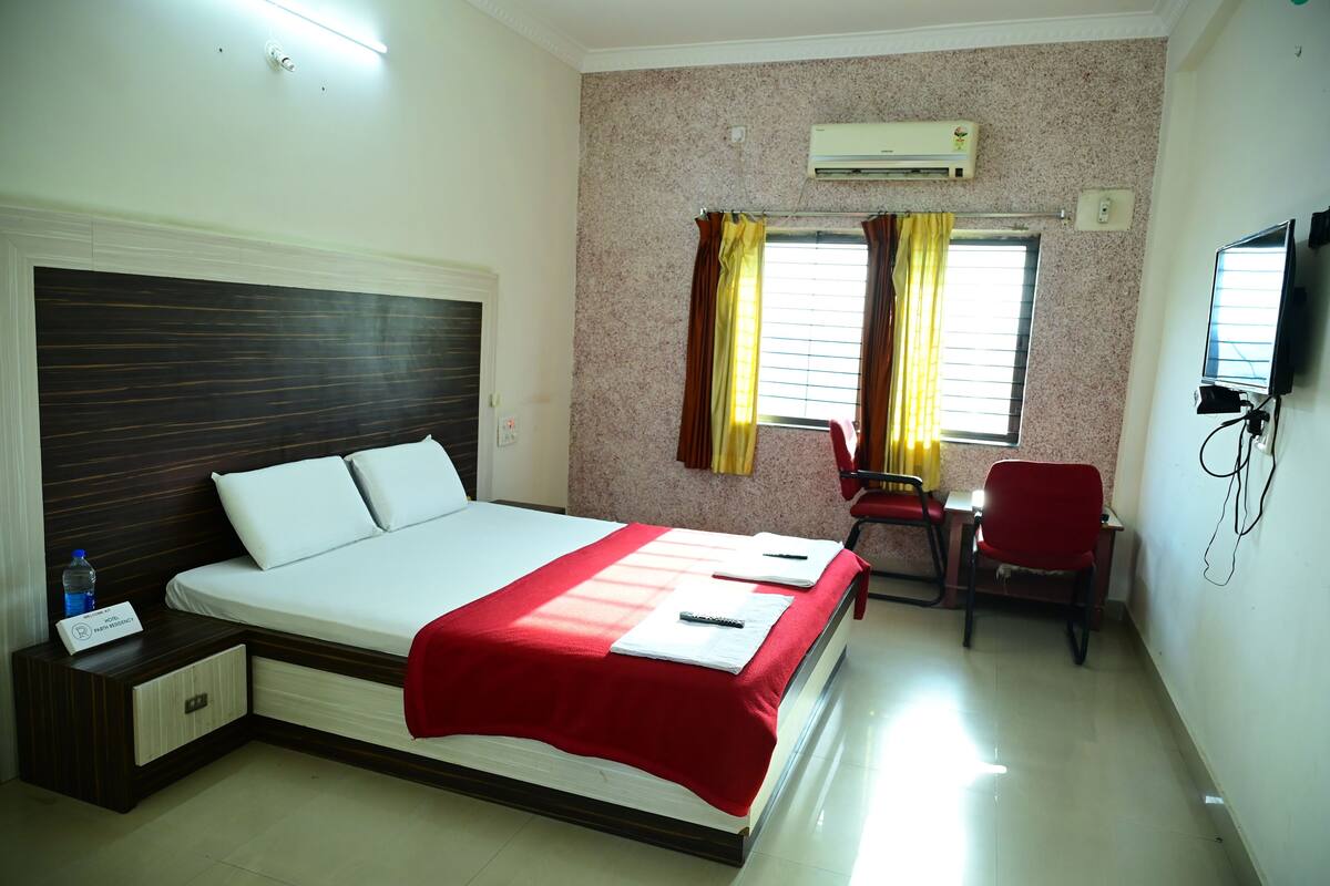 A hotel room with a bed, a desk with a chair, an air conditioner, and a television.