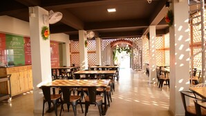Un comedor amplio con varias mesas y sillas, una barra con un menú y elementos decorativos como flores y paneles estampados.