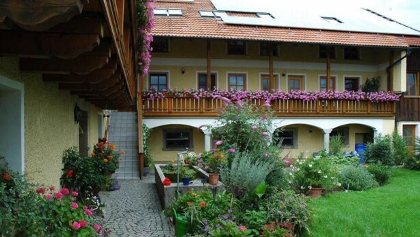 A traditional building with a balcony, a garden with various plants, and a cobblestone pathway. - Ferienhof Löw (Salzweg)