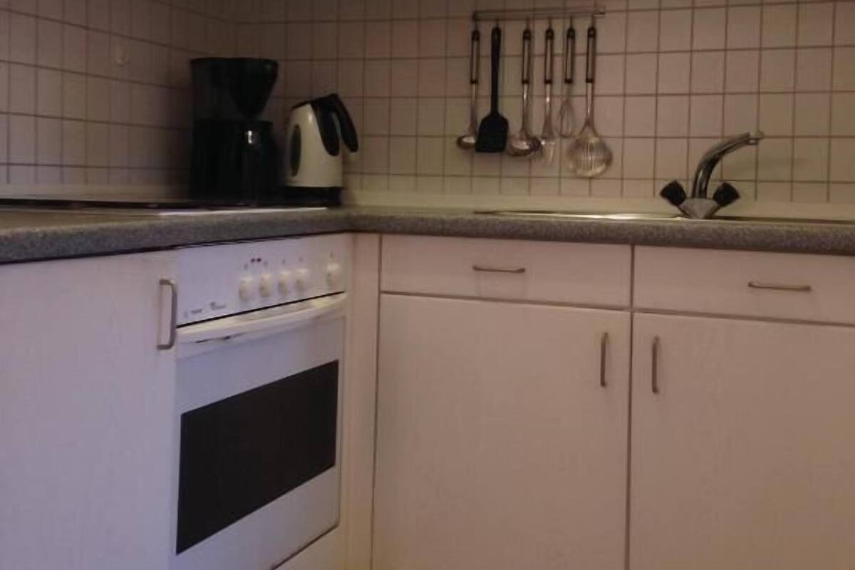 A kitchen with white cabinets, a stove, a coffee maker, and a sink.