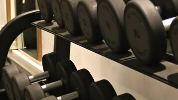 A rack of black dumbbells with weight markings, arranged on a shelf in a gym.