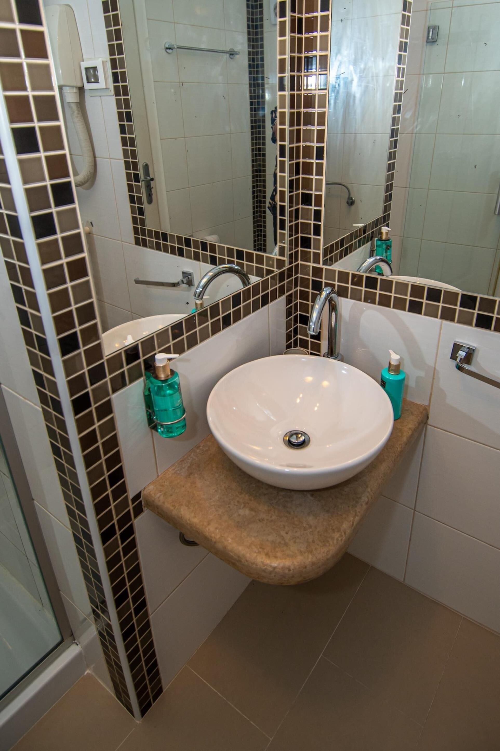 Un baño con lavamanos blanco, espejo y zona de ducha.