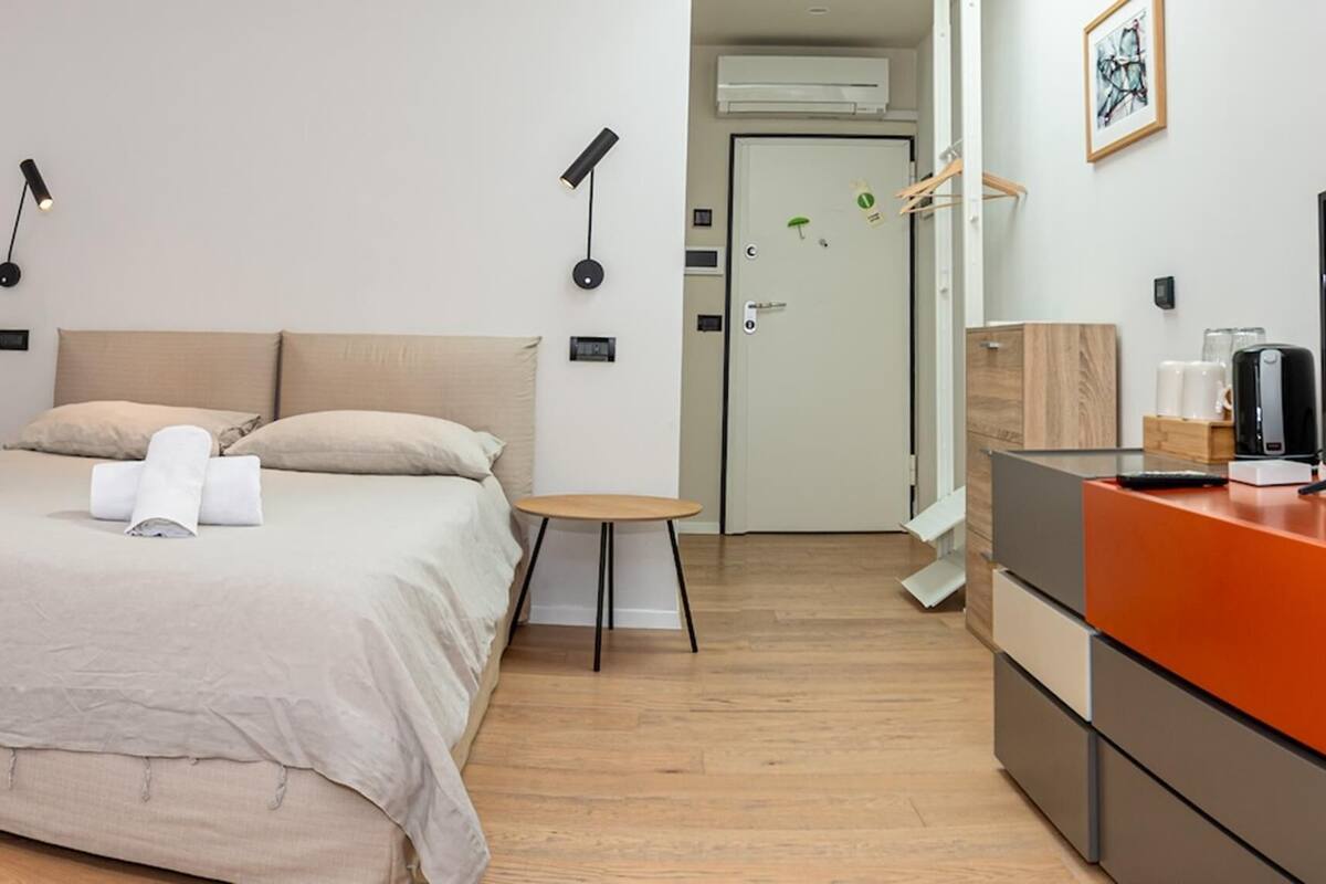 Una habitación de hotel moderna con una cama grande, una mesa redonda, un televisor y un espejo.
