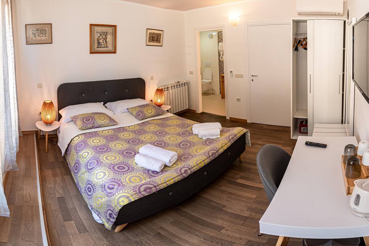 Habitación de hotel con una cama, lámparas de noche, un escritorio con hervidor y tazas, y un armario.