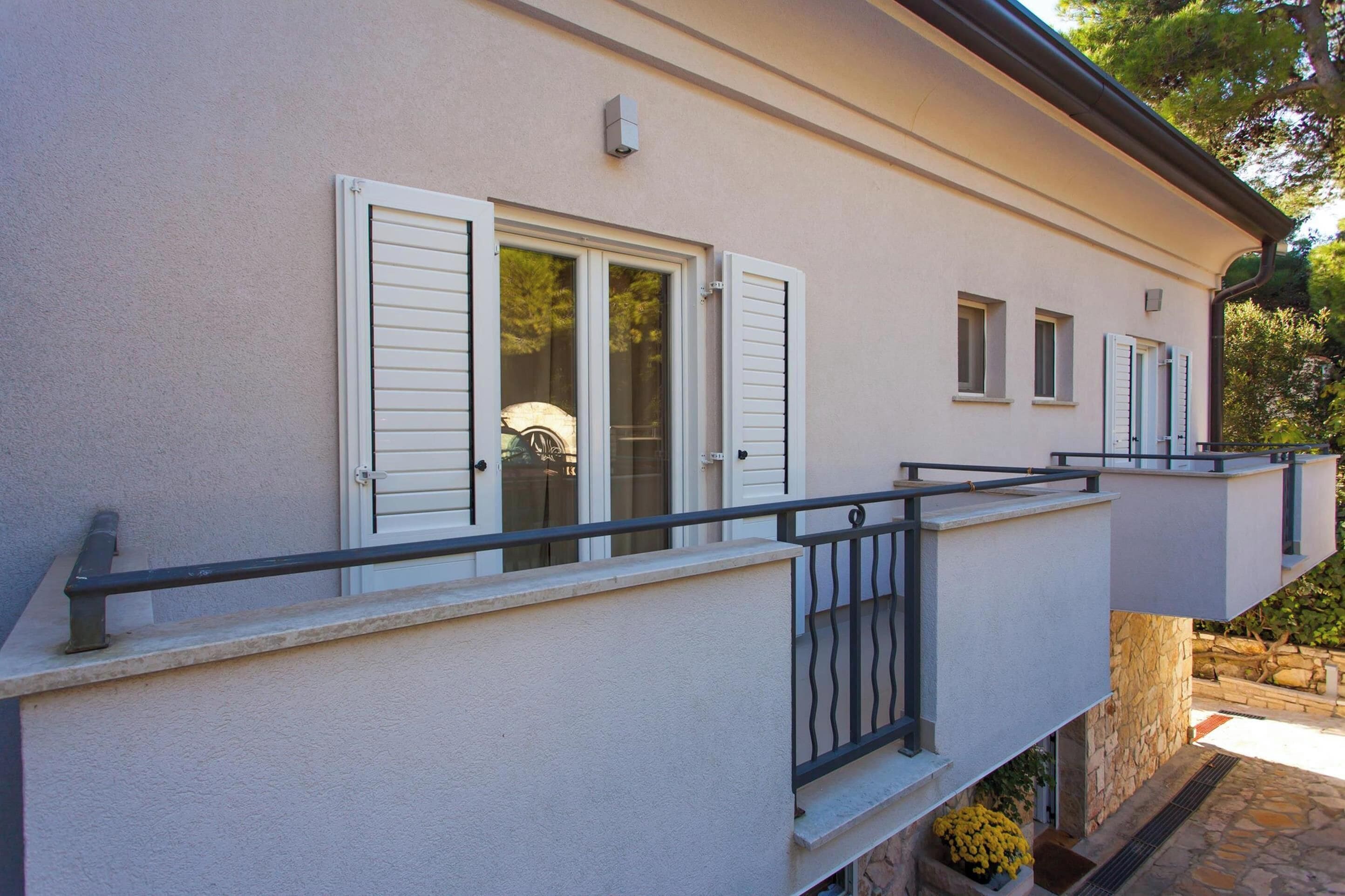 A building with a balcony, white shutters, and a stone foundation.