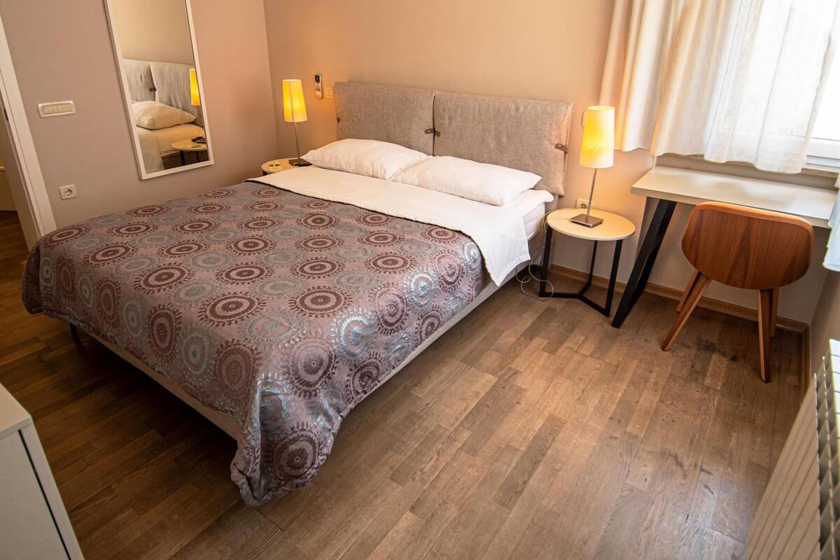 Un dormitorio con cama, lámparas de noche, una mesita y una silla.