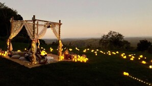Un entorno exterior con una estructura tipo toldo, mantas, almohadas y luces colgantes.