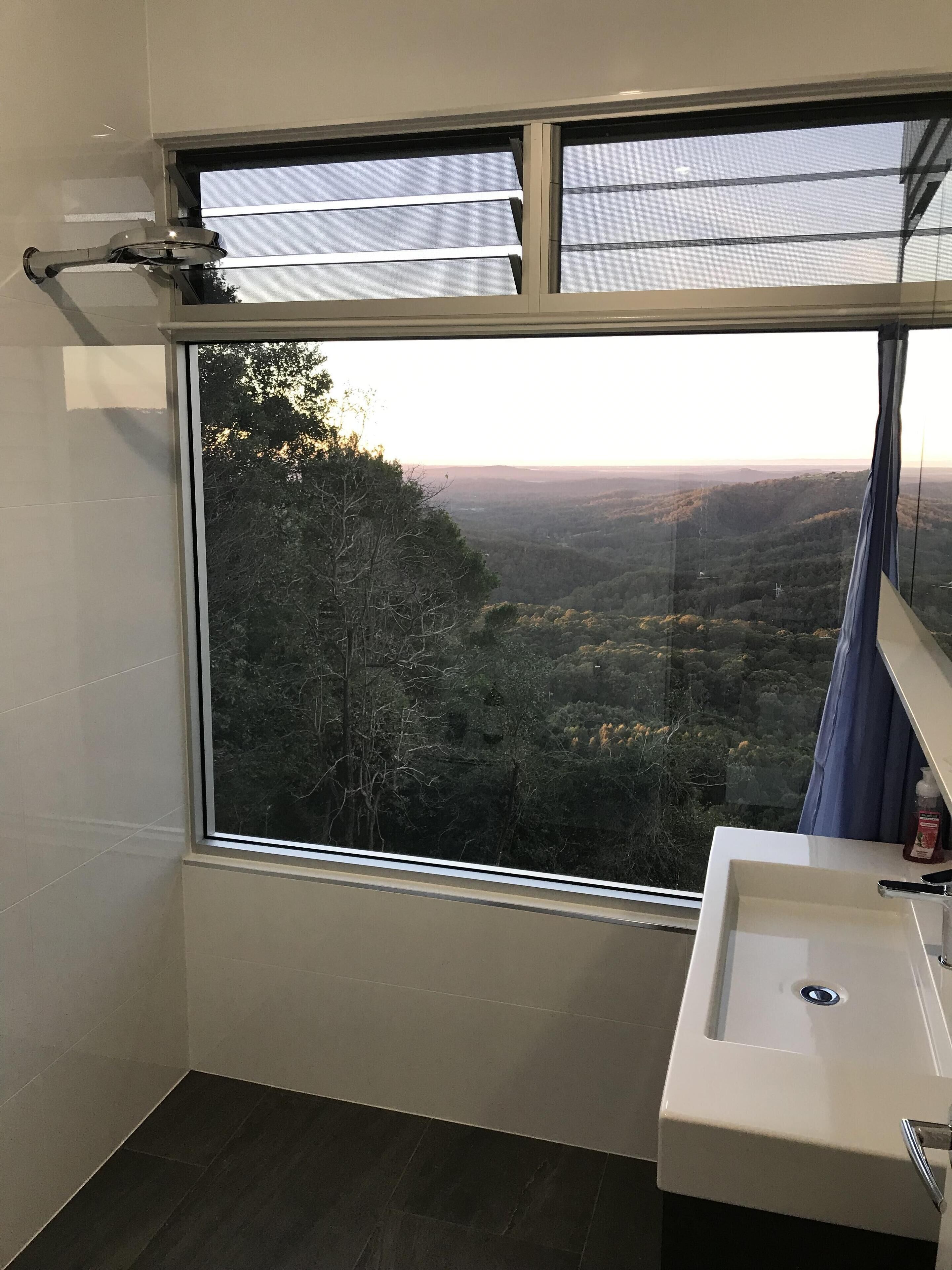Een badkamer met een groot raam en uitzicht op een bebost landschap.