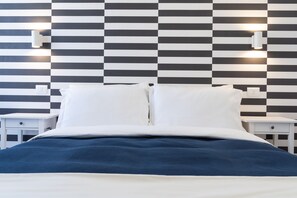 Een netjes opgemaakt bed met wit- en blauwe beddengoed, twee nachtkastjes en een geruit behang.