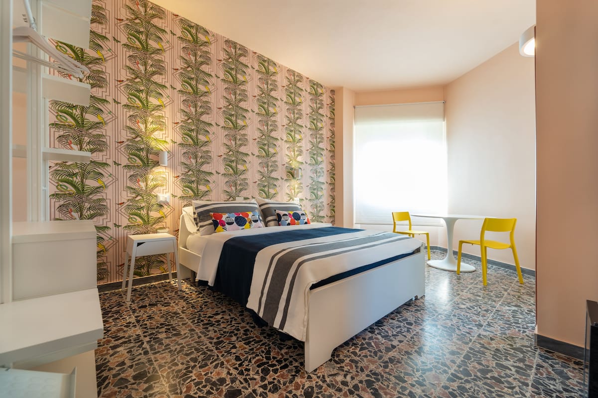 Une chambre d’hôtel avec un lit, une petite table, deux chaises, un escalier et un papier peint à motifs.