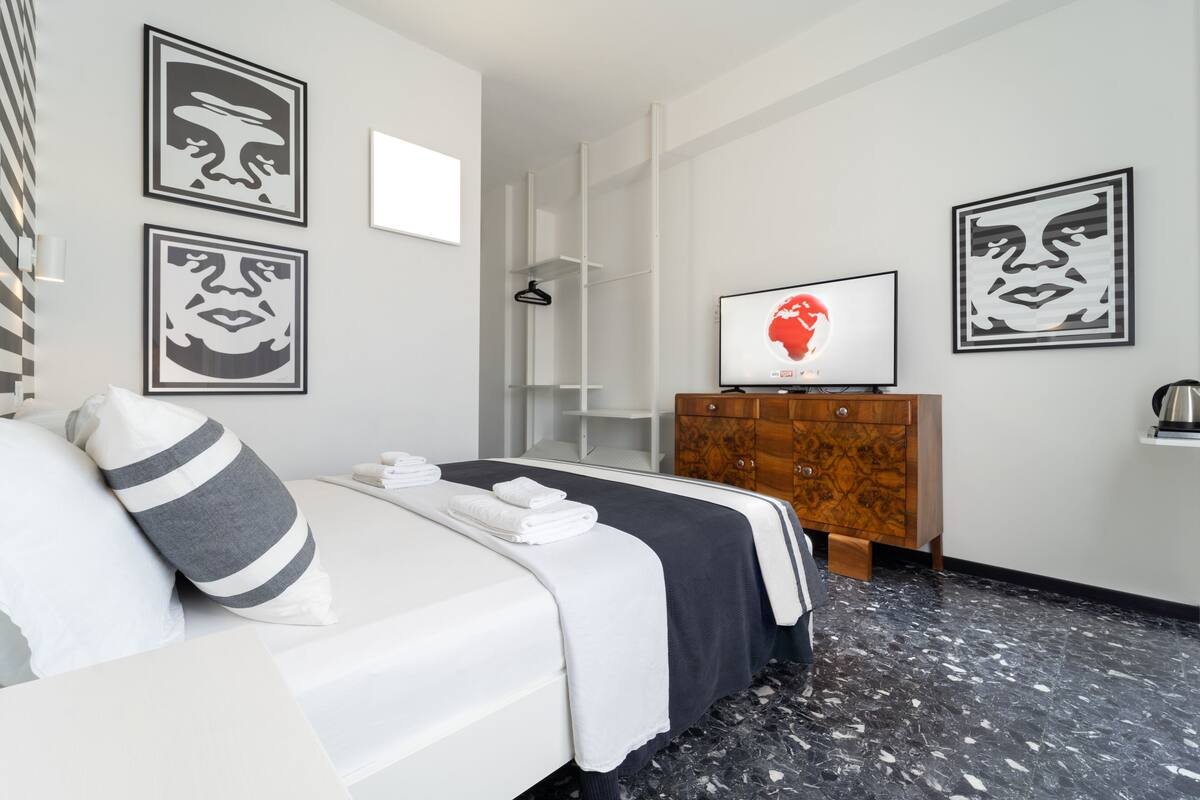 Une chambre d’hôtel avec un lit, une commode en bois, une télévision et des œuvres d’art accrochées aux murs.