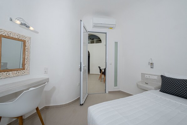 A bedroom with a bed, a desk, a chair, a mirror, and an open door leading to a bathroom.