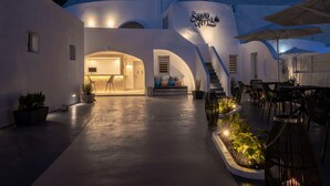 A modern building with a sign reading "Santo Yvaria." It features a spacious outdoor area with seating and potted plants. - Santoterra Antigua Suites (Santorini)