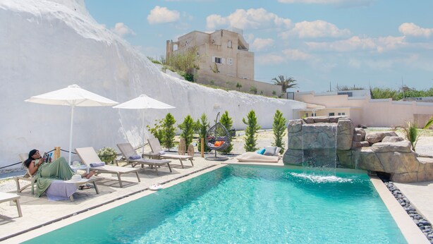 A pool area with lounge chairs, umbrellas, and a waterfall feature. - Santoterra Antigua Suites (Santorini)