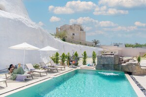 Ein Poolbereich mit Liegestühlen, Sonnenschirmen und einem Wasserfall.
