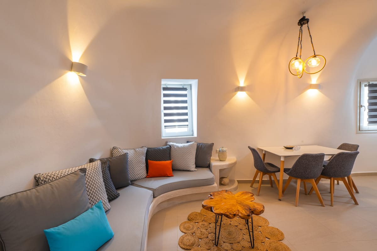 Een moderne woonkamer met een gebogen bank, een eettafel met stoelen en wandlampen.