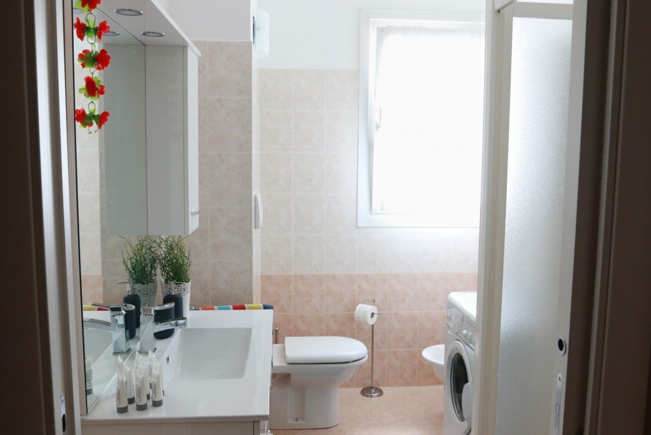 A modern bathroom with a glass shower enclosure, a toilet, a washing machine, and a sink with a mirror.
